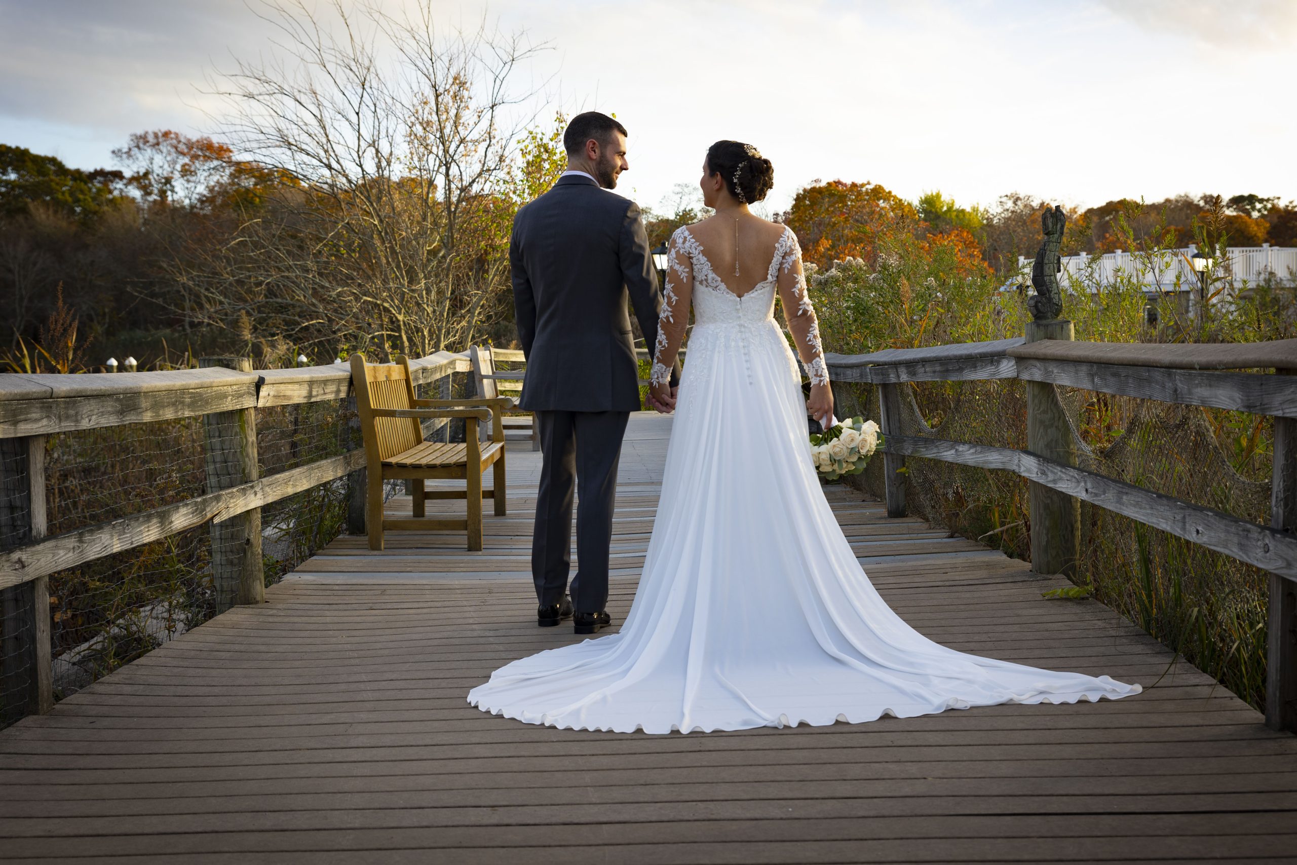 Bride and groom stand on boardwalk with fall foliage in the background
